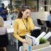 Frustrated young woman in yellow sweater standing at table and touching face with hand while packing stuff in office after dismissal
