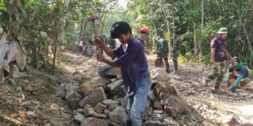 Seorang warga bersama personel Satgas TMMD Ke-129 Kodim 0601/Pandeglang memecahkan batu menggunakan martil sebagai material pengerasan jalan di Kampung Ciririgi, Desa Simpangtiga, Kecamatan Patia, Kabupaten Pandeglang.