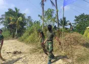 Personel Satgas TMMD melaksanakan pembersihan rumput dan semak belukar di sekitar tenda posko guna menciptakan lingkungan yang bersih, aman, dan nyaman selama pelaksanaan Program TNI Manunggal Membangun Desa (TMMD).