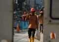 Dikebut di Balik Pagar Seng, Pekerja MRT Fase 2A Pacu Konstruksi Stasiun Glodok 6 PROYEK MRT GLODOK: Seorang pekerja konstruksi memikul balok kayu penyangga dan menjinjing karung material di area pembangunan stasiun bawah tanah MRT Jakarta Fase 2A Paket Kontrak CP203 di depan gerbang Pasar Glodok, Jalan Gajah Mada, Tamansari, Jakarta Barat, Minggu (18/10/2026). Pengerjaan struktur sipil stasiun bawah tanah koridor Bundaran HI–Kota tersebut terus dikebut guna mengejar target konektivitas transportasi massal kawasan Kota Tua. (Foto: Rachmat Yoga Pradika)